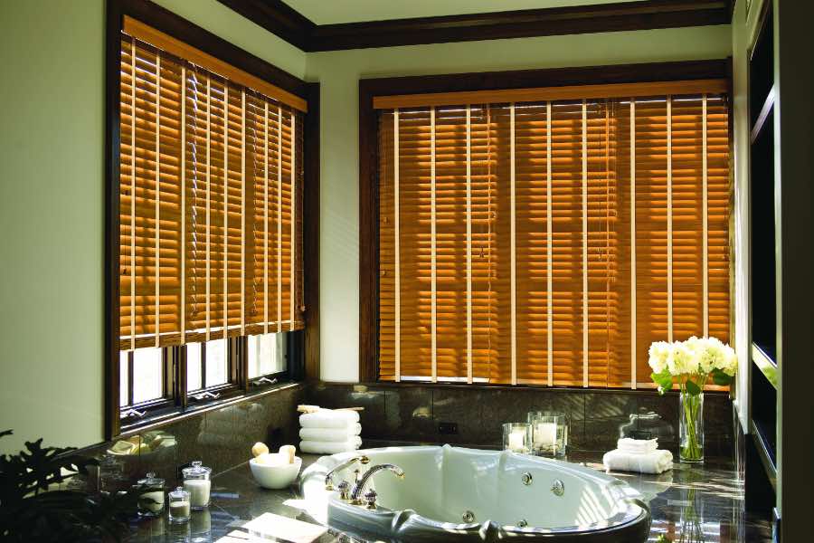 Premium quality blinds are always a stylish accent in your San Antonio home. Brown wood blinds on large windows in a green bathroom
