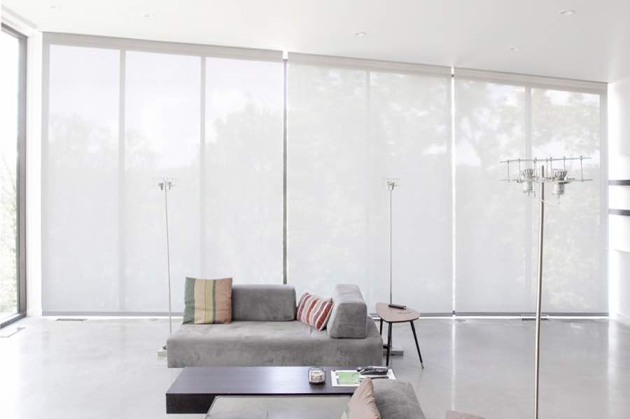 Motorized window shades make controlling natural light effortless in your San Antonio great room. White motorized shades on a wall of tall great room windows