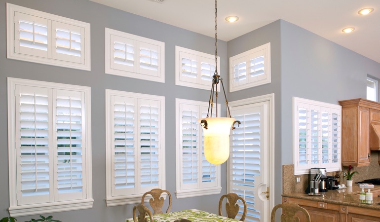 Plantation shutters can resolve both sun glare and heat loss problems. White plantation shutters in dining room