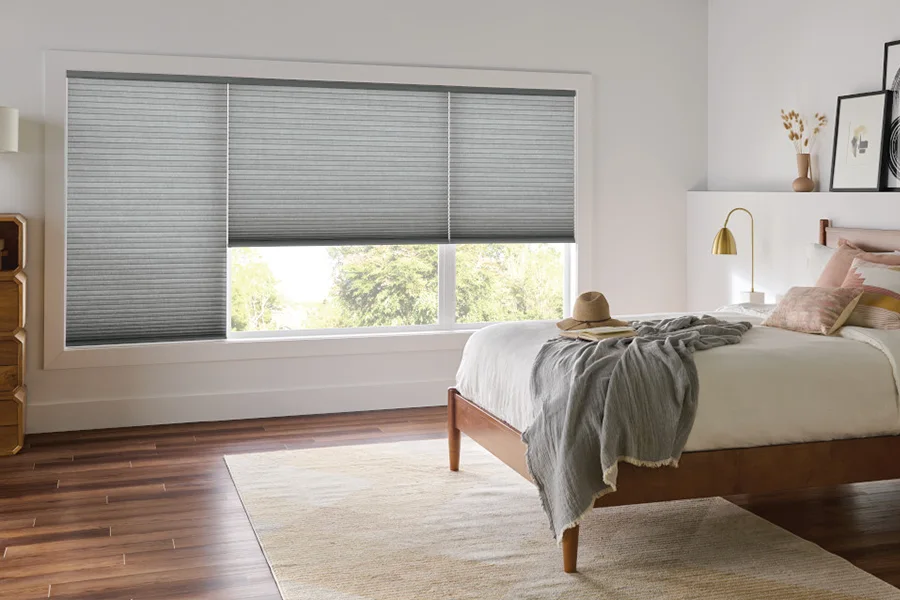 The honeycomb-like pockets of cellular shades trap air to improve energy efficiency. ash gray cellular shades on three large windows within a modern farmhouse style bedroom