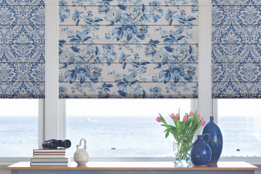Beautiful new window treatments make windows even more eye-catching. Blue and white patterned Roman shades on a window overlooking the ocean