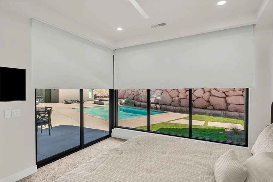 Boost energy efficiency by scheduling motorized shades to close automatically during peak sun hours. Motorized white window shades covering large bedroom windows